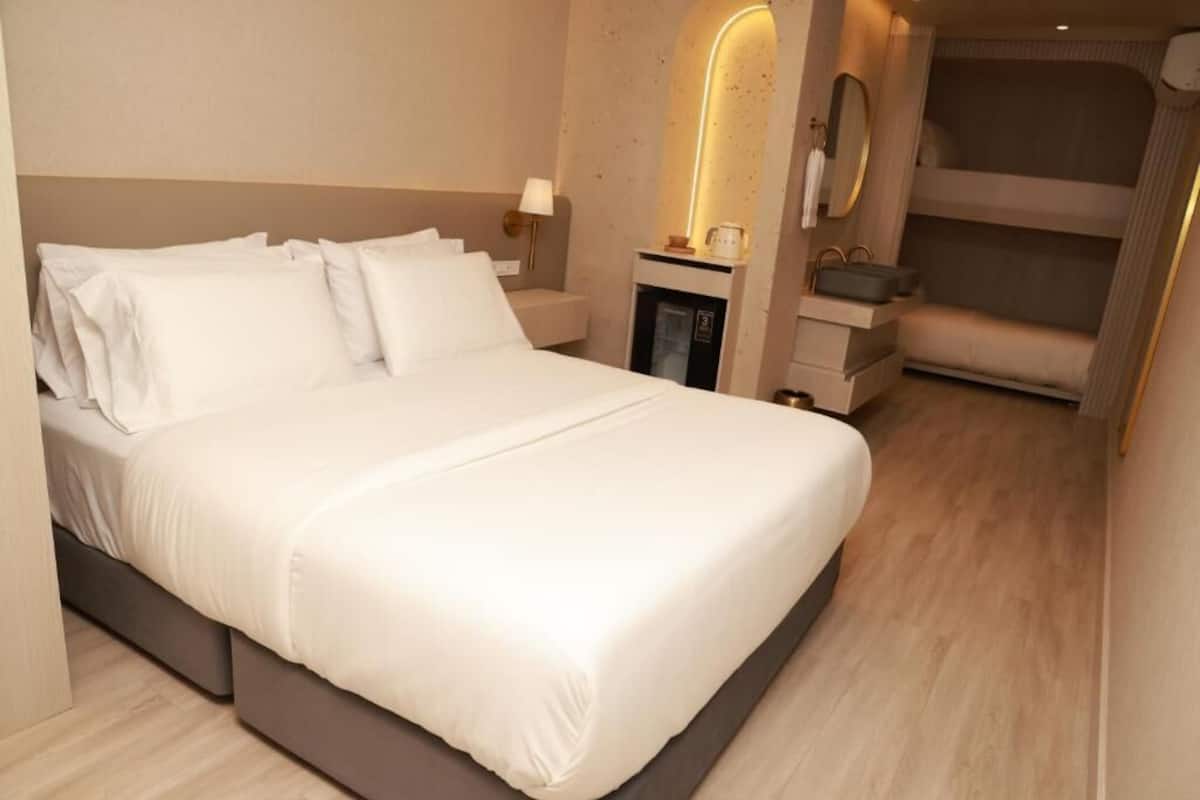 A modern hotel room with a large bed, a bedside table, a mirror, and a built-in bench with storage.
