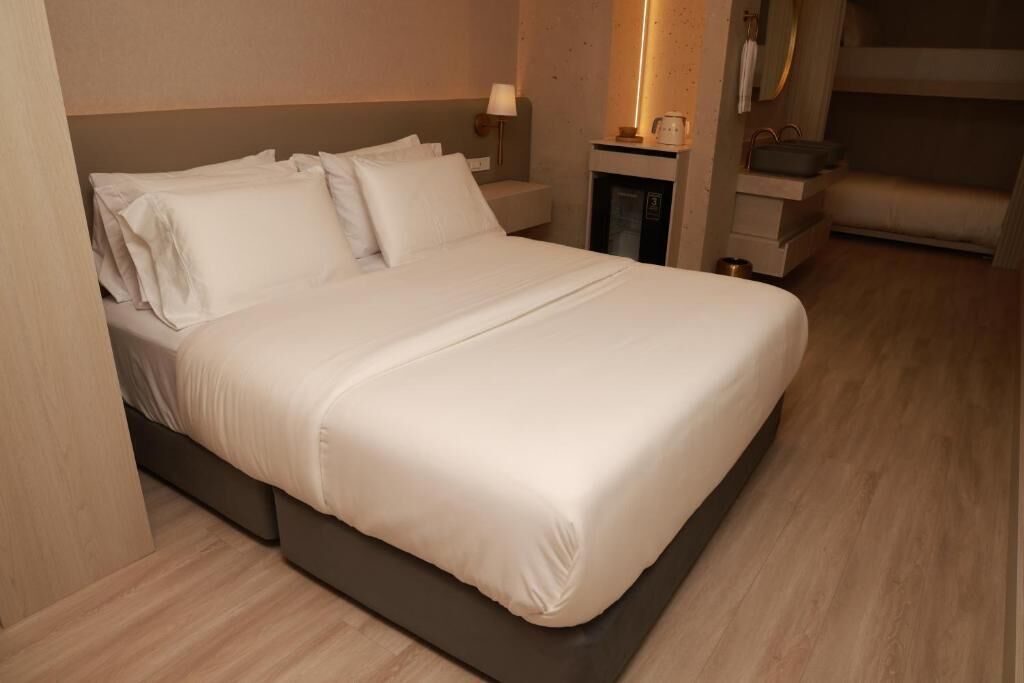 A neatly made bed with white linens, a bedside table with a lamp, and a small cabinet.