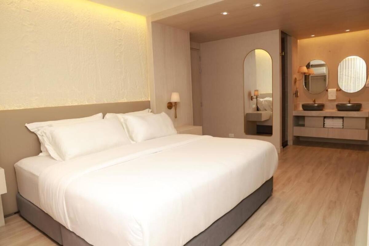 A modern hotel room with a large bed, a bathroom with a vanity, and a mirror.
