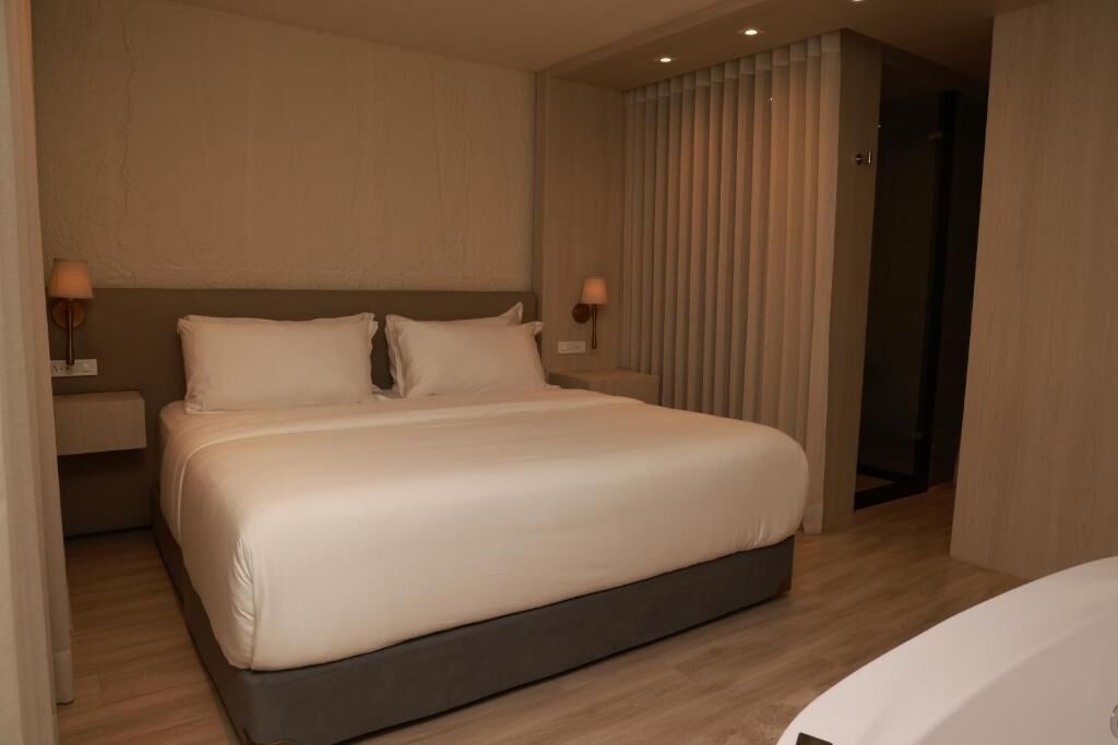A modern hotel room with a large bed, two bedside tables, and a nightstand.