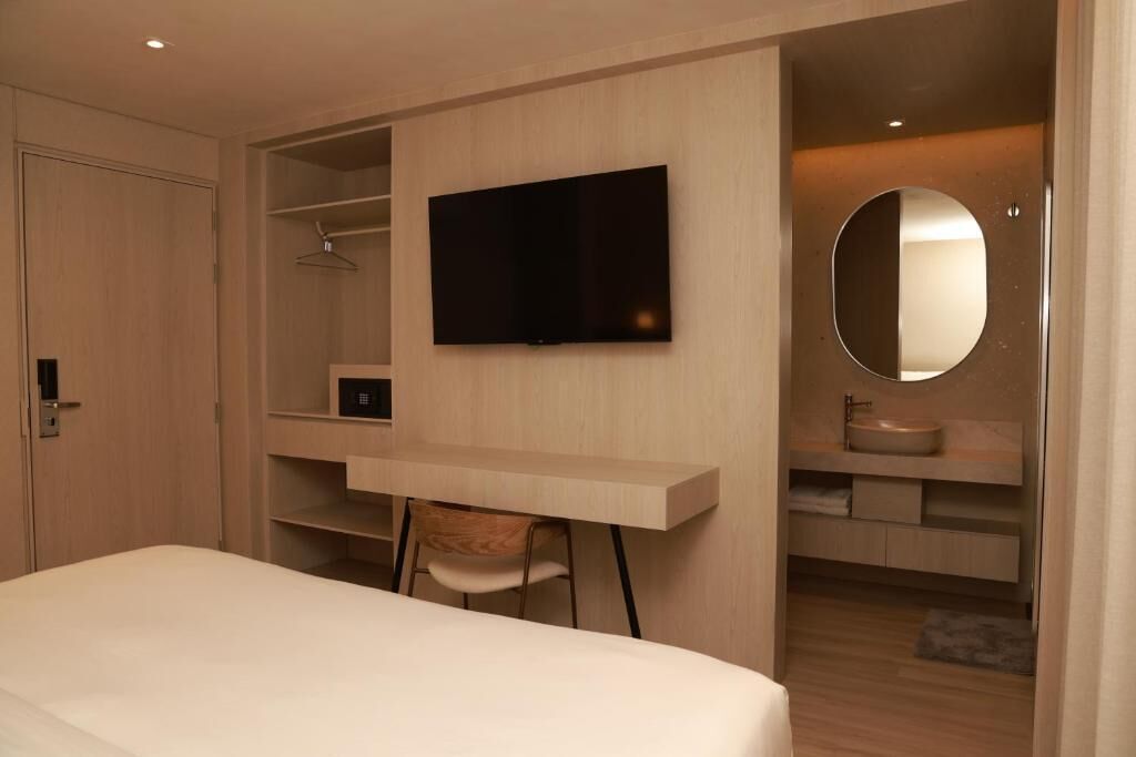 A modern bedroom with a bed, a desk, a TV, and a bathroom with a mirror and sink.