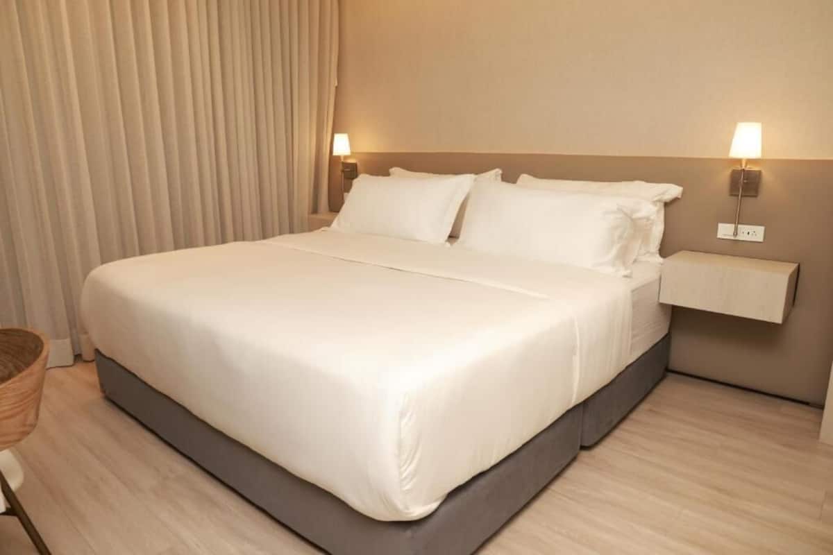 A neatly made bed with white linens in a hotel room.