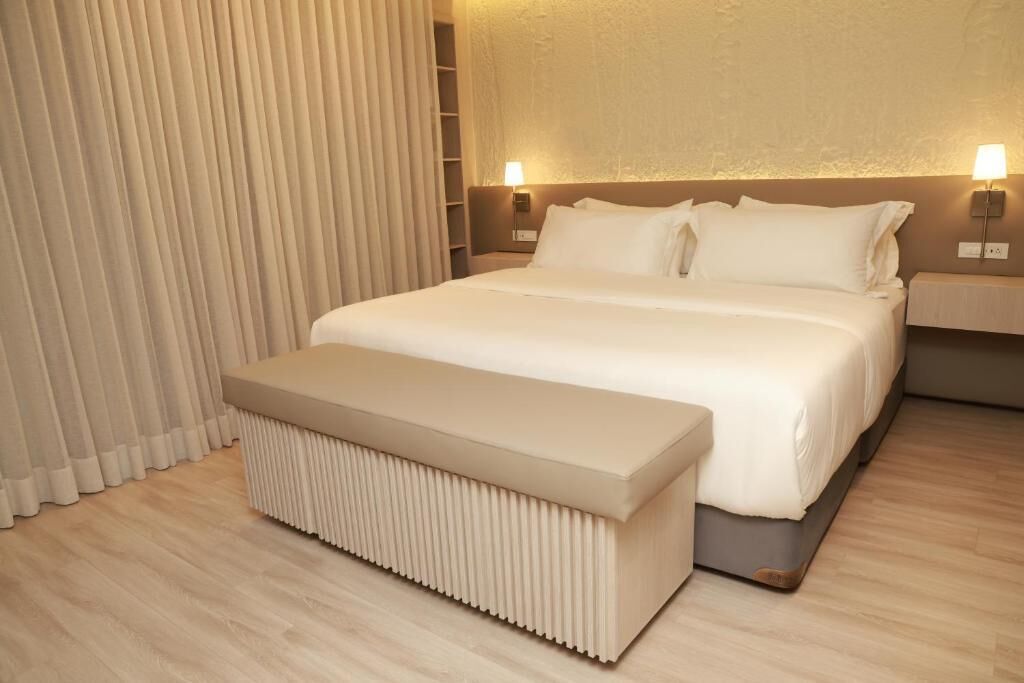 Une chambre d’hôtel moderne avec un grand lit, des tables de chevet et un banc.
