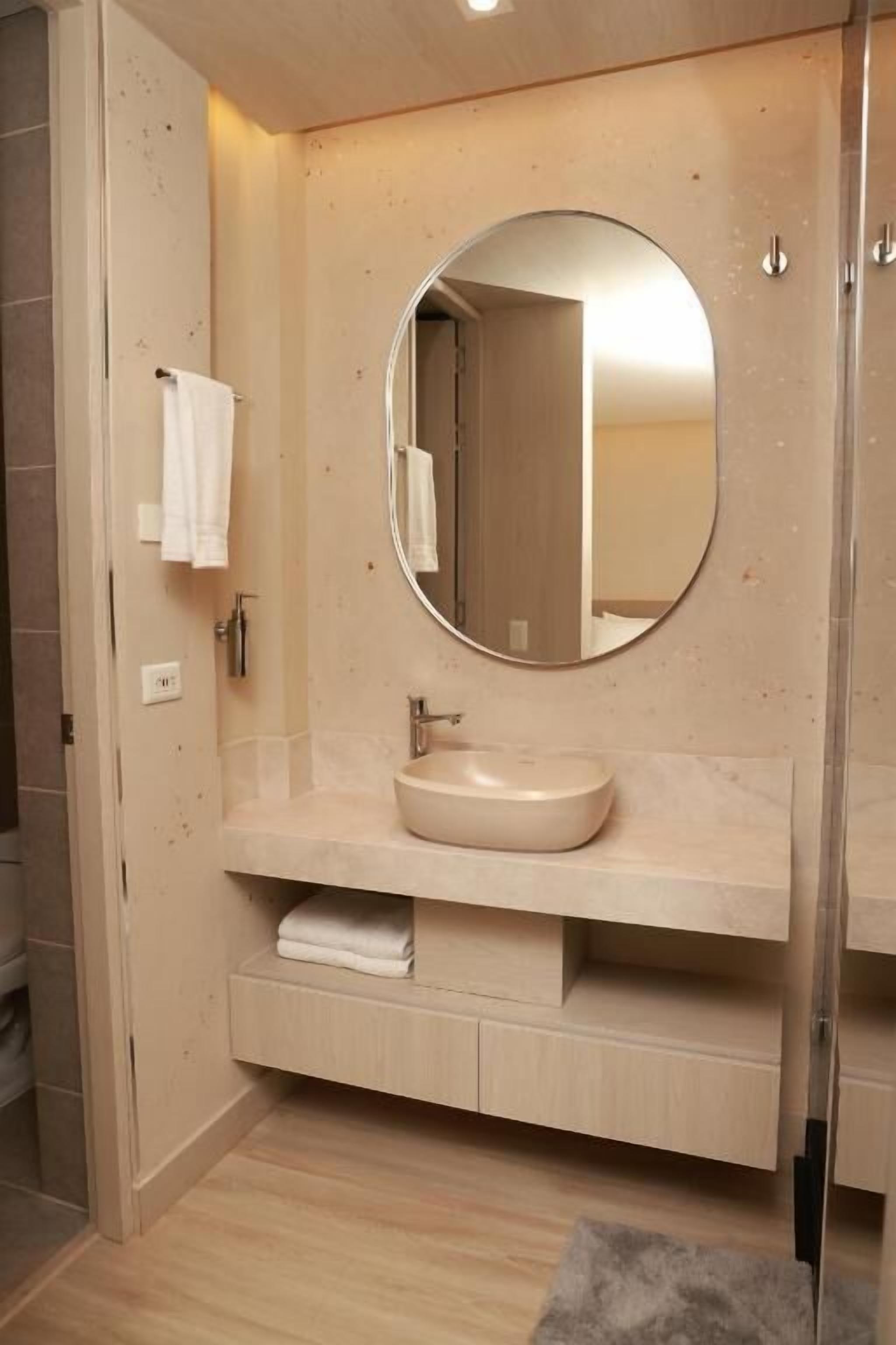 A modern bathroom with a round mirror, a beige sink, and a towel rack.