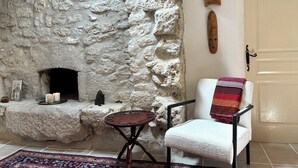 A stone fireplace with a white chair and a small table in front. - La Muse Rossignol: Swimming pool, spacious rooms & private bath in Occitanie (Belvèze)