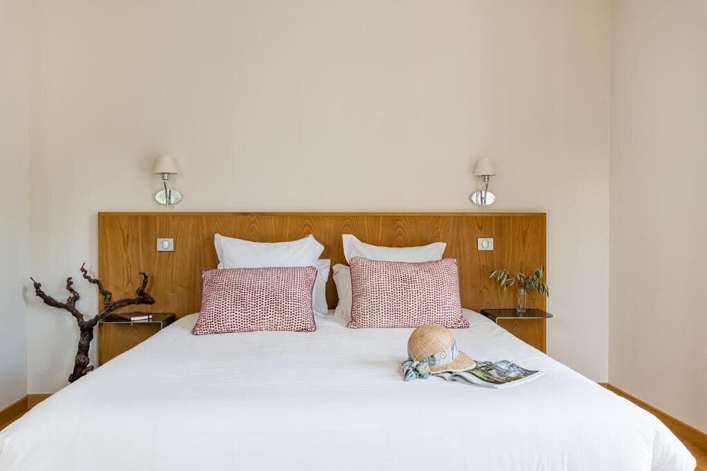 Ein ordentlich bezogenes Bett mit weißen und roten Kissen, einem Holz-Kopfschild und zwei Nachttischlampen.