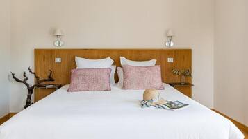 Ein ordentlich bezogenes Bett mit weißen und roten Kissen, einem Holz-Kopfschild und zwei Nachttischlampen.