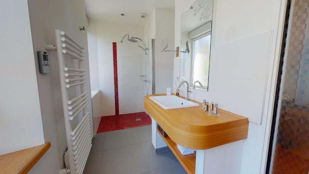 Un baño moderno con tocador de madera, un espejo grande y zona de ducha.