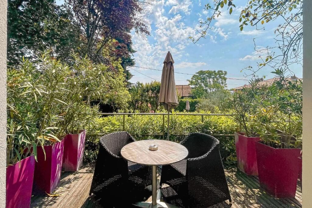 An outdoor patio with a round table and two chairs, surrounded by potted plants and a large umbrella.