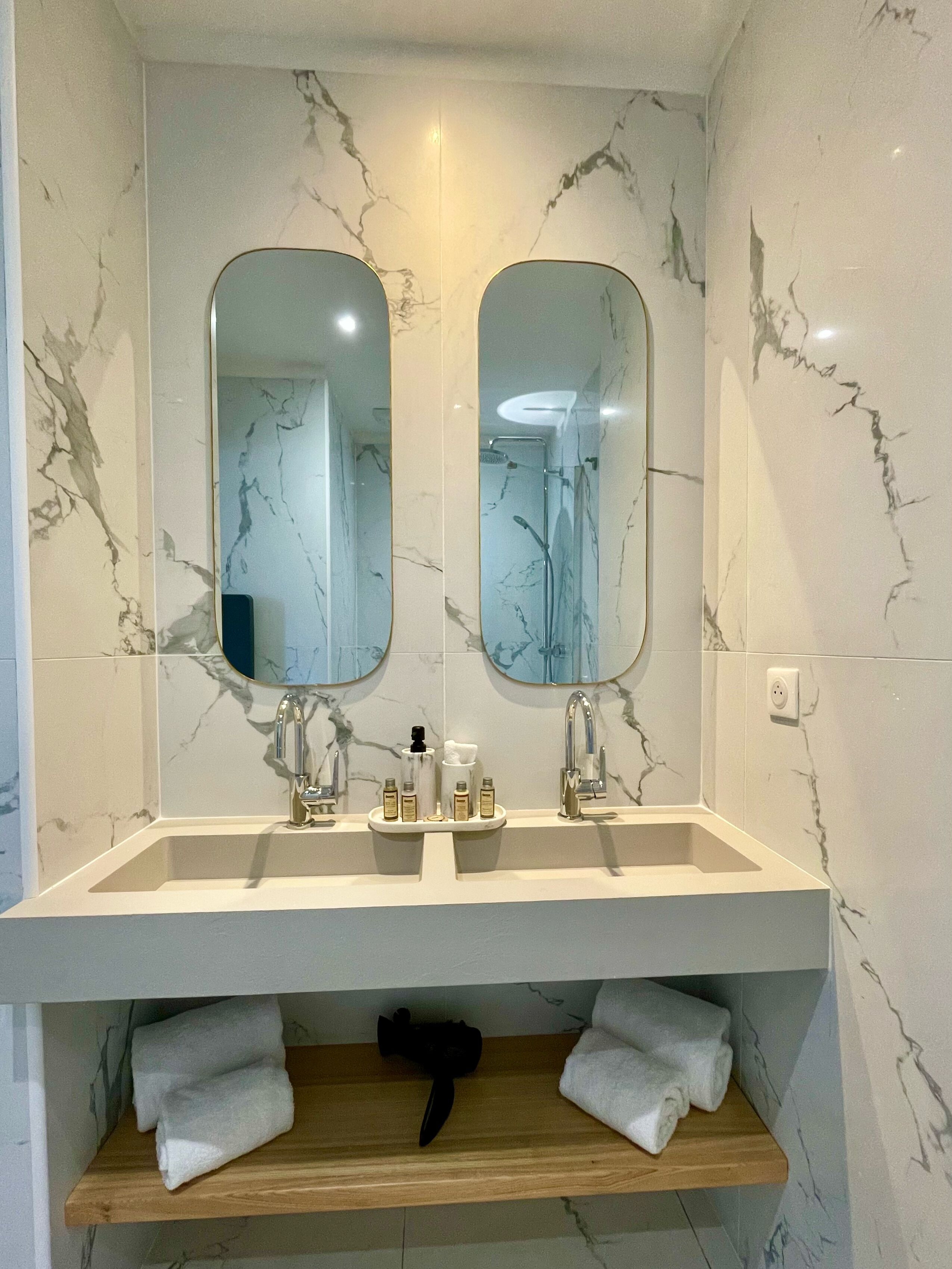Ein Badezimmer mit zwei Waschbecken, Marmorwänden und einem Holzregal mit Handtüchern.