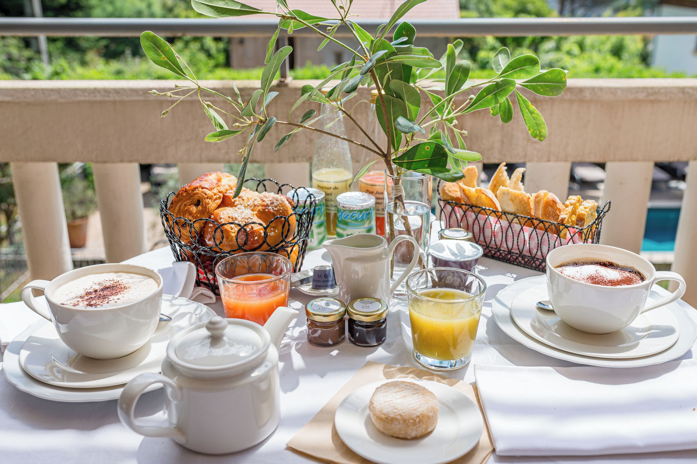 Un petit-déjeuner préparé avec des viennoiseries, du café et du jus, servi sur une table à l’extérieur, avec vue sur la verdure.