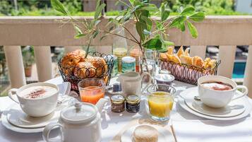 Un petit-déjeuner préparé avec des viennoiseries, du café et du jus, servi sur une table à l’extérieur, avec vue sur la verdure.