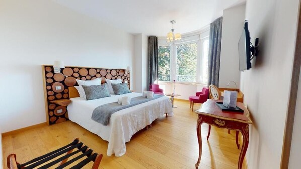 Une chambre à coucher comprenant un lit, une tête de lit en bois, une table de chevet, une chaise, un bureau et une fenêtre avec des rideaux.