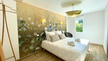 A bedroom with a bed, a wall-mounted lamp, a window, and a wooden floor.