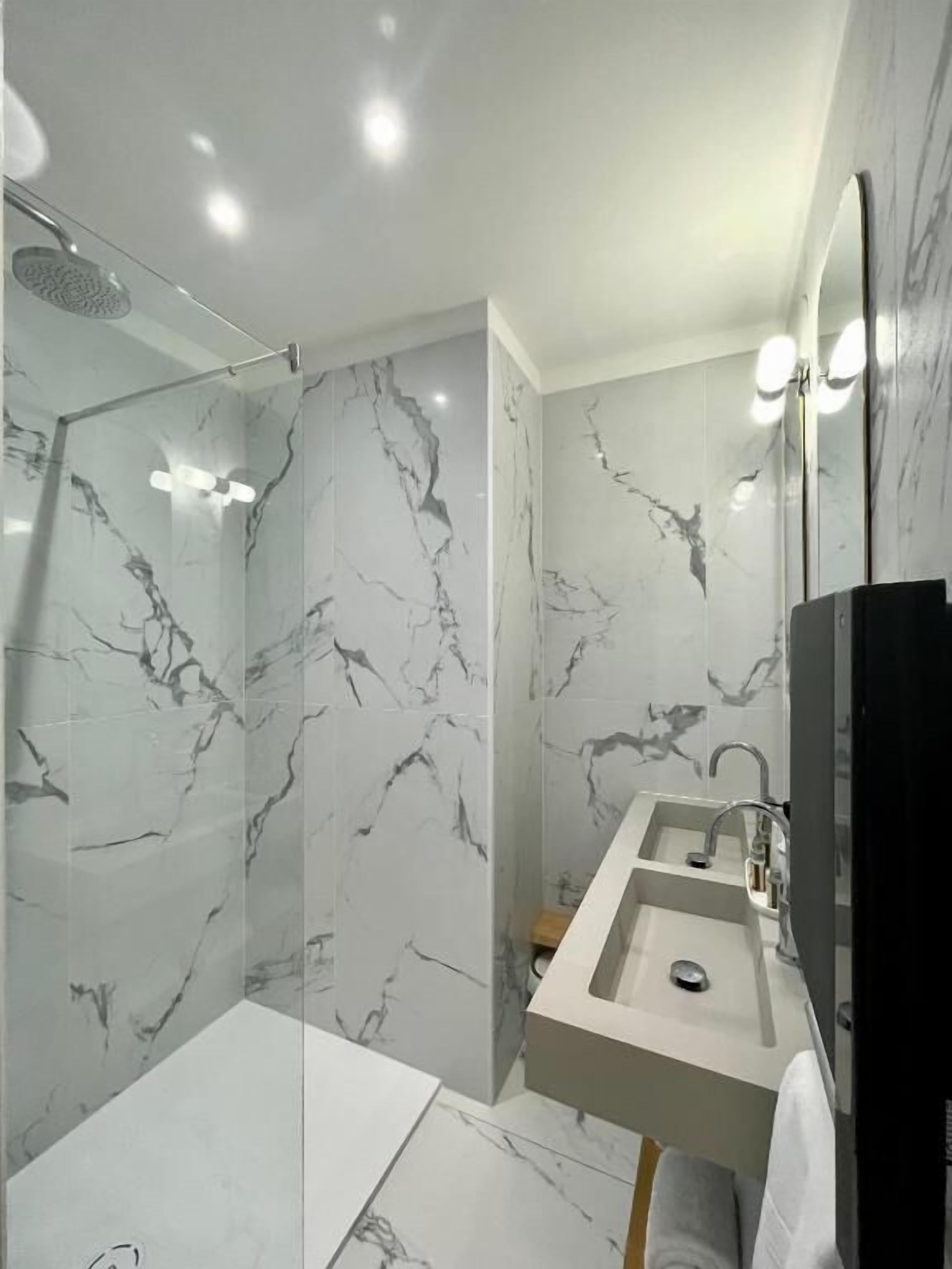 Un baño moderno con paredes de mármol, cabina de ducha de vidrio, tocador doble y un espejo grande.
