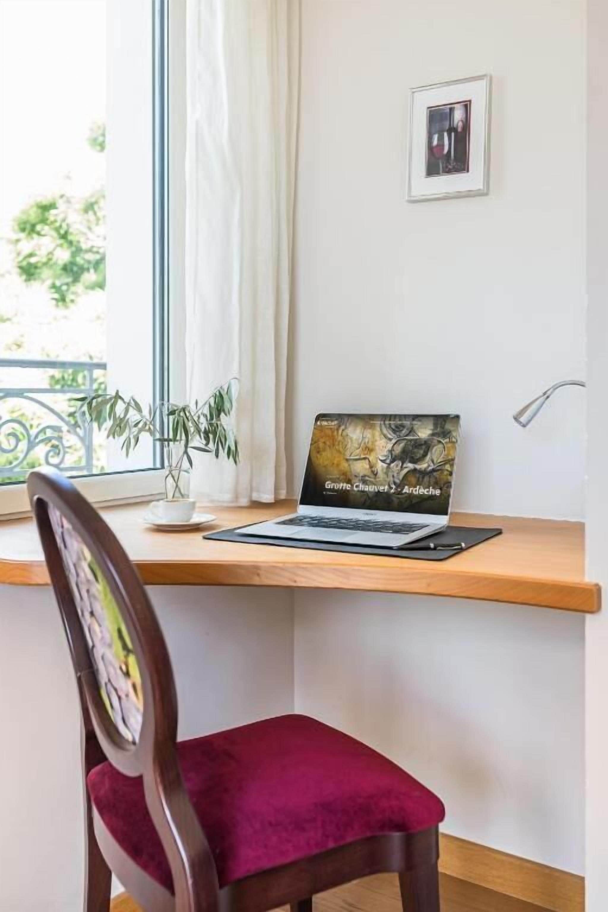 A workspace with a laptop, a chair, a potted plant, and a framed picture on the wall.
