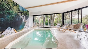 Ein Swimmingpool mit Wandgemälde eines Wasserfalls, Liegestühlen und großen Fenstern.