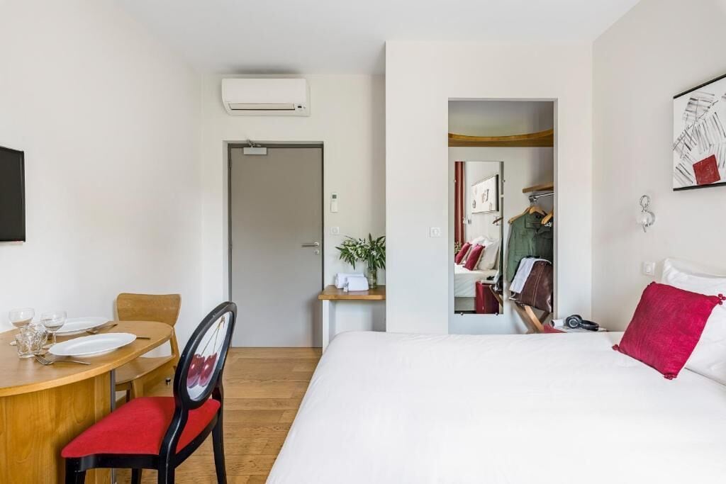 Una habitación de hotel con una cama, un escritorio con silla, un espejo y un armario.