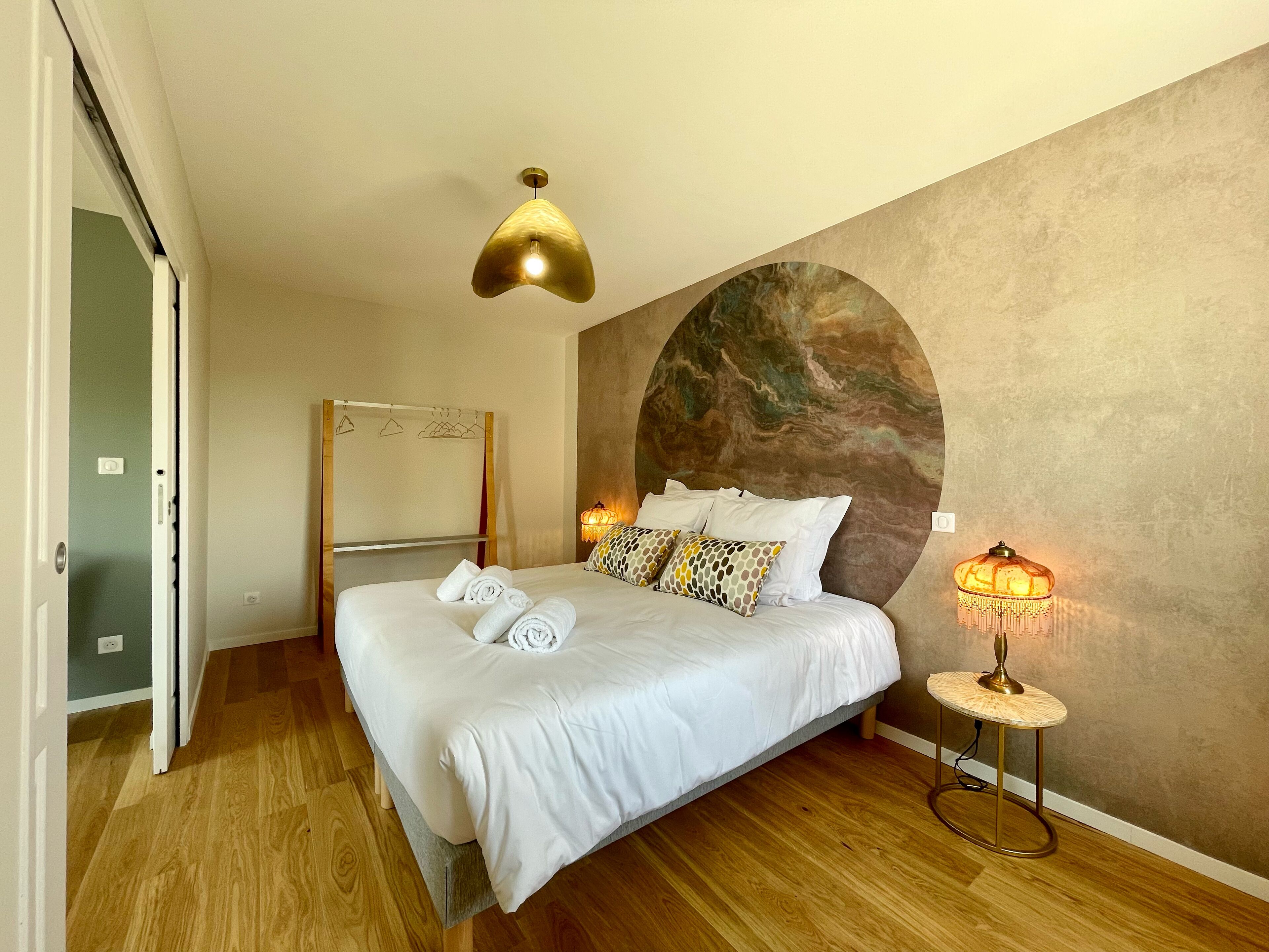 A hotel room with a bed, a bedside table with a lamp, a mirror, and a wall with a circular design.