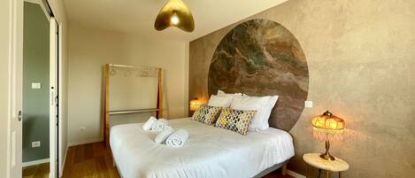 Habitación de hotel con cama, mesita de noche con lámpara, espejo y pared con diseño circular.