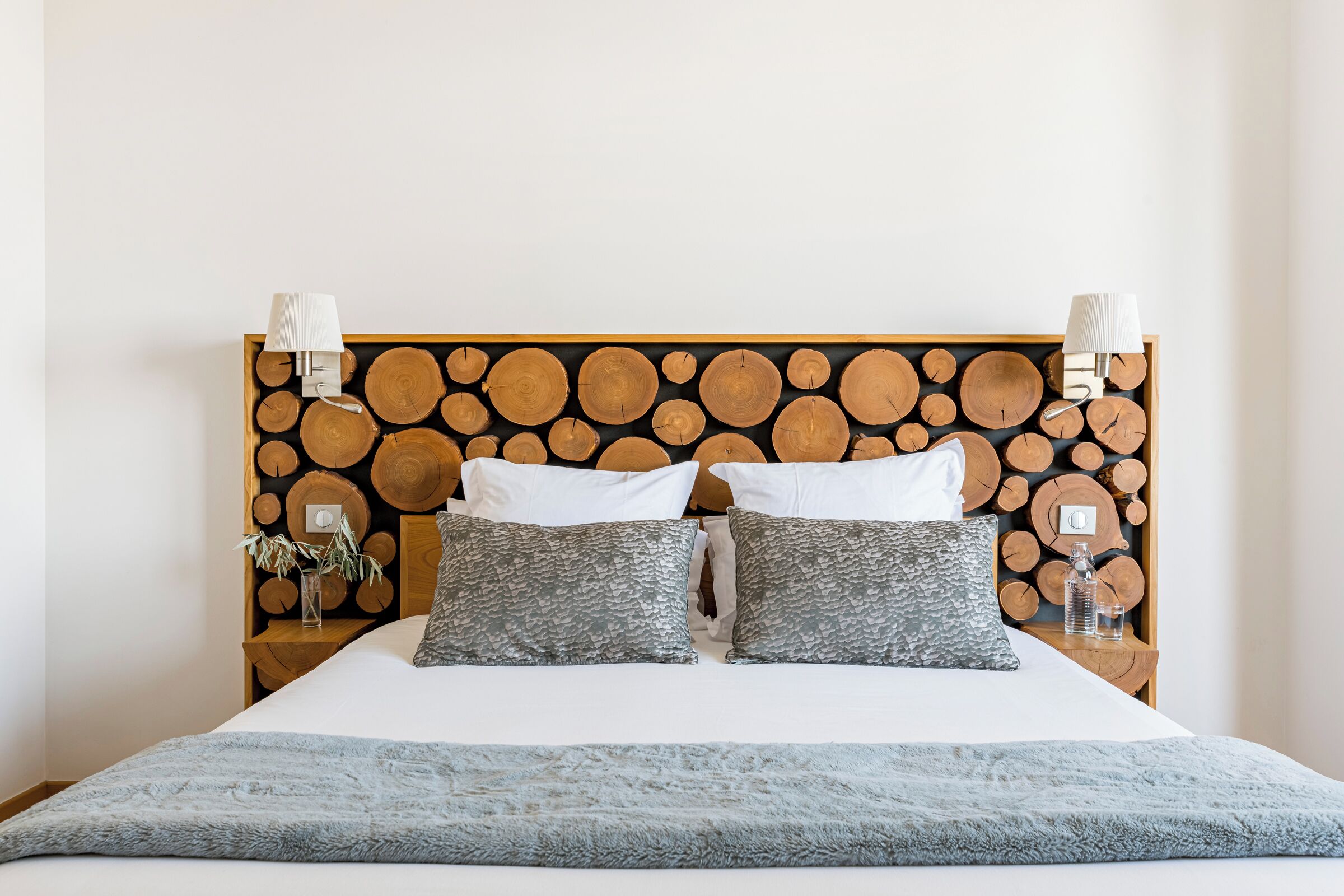 A bed with a wooden headboard, two white pillows, two gray patterned pillows, and a blue blanket.