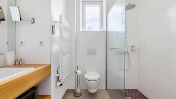 Et moderne badeværelse med en trækommode, toilet, brusekabine i glas og et vindue over toilettet.