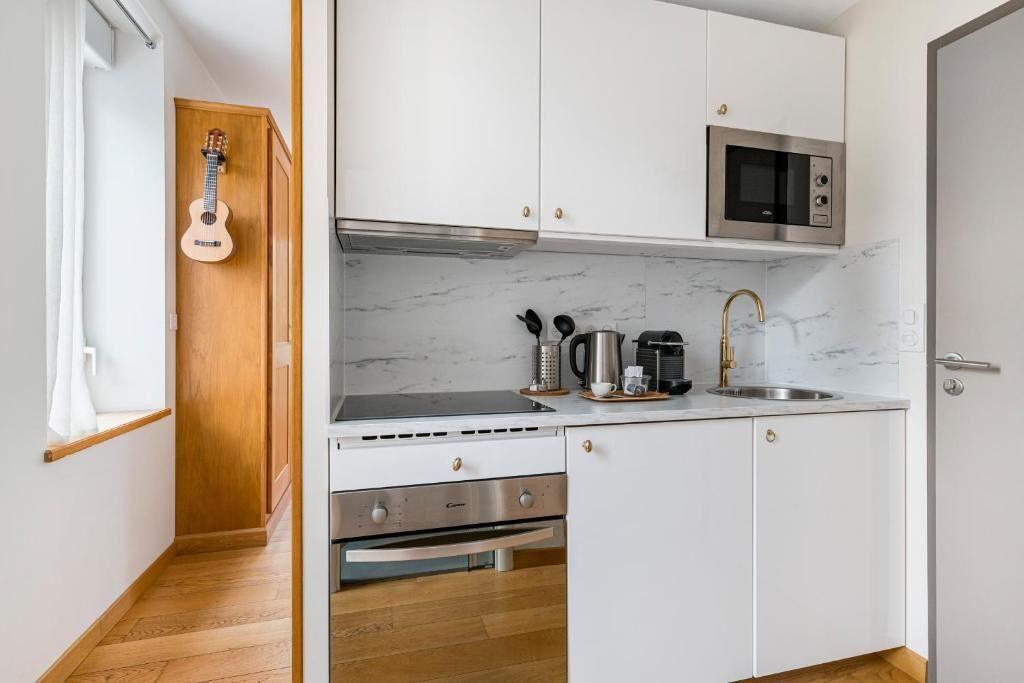 Een kleine keuken met witte kastjes, een ingebouwde magnetron, een gasfornuis en een spoelbak.