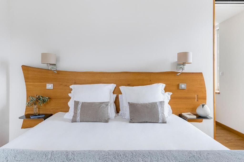 A neatly made bed with a wooden headboard, two bedside tables with lamps, and a small plant on one table.