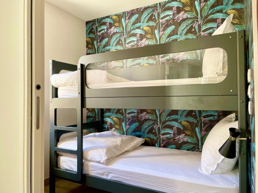 A bunk bed with a floral wallpaper, a white pillow, and a black vase on the side.