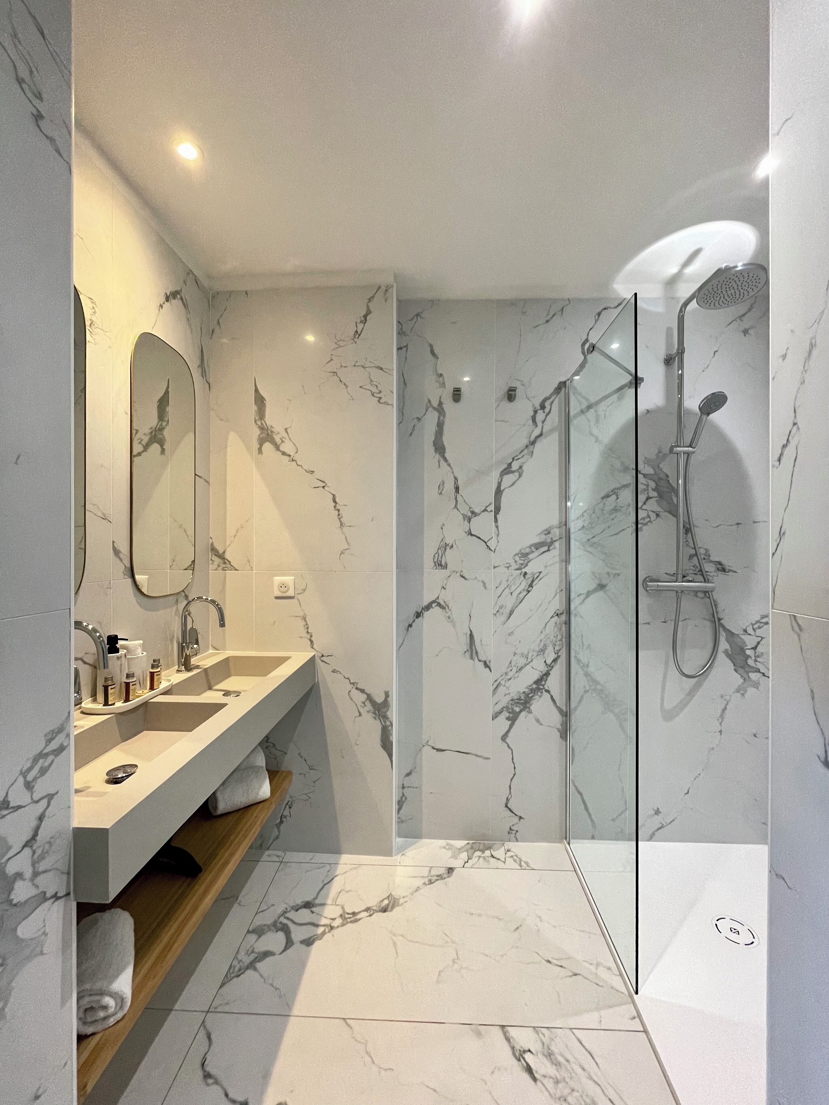 A modern bathroom with a marble backsplash, a double sink vanity, a glass shower enclosure, and a built-in shelf.