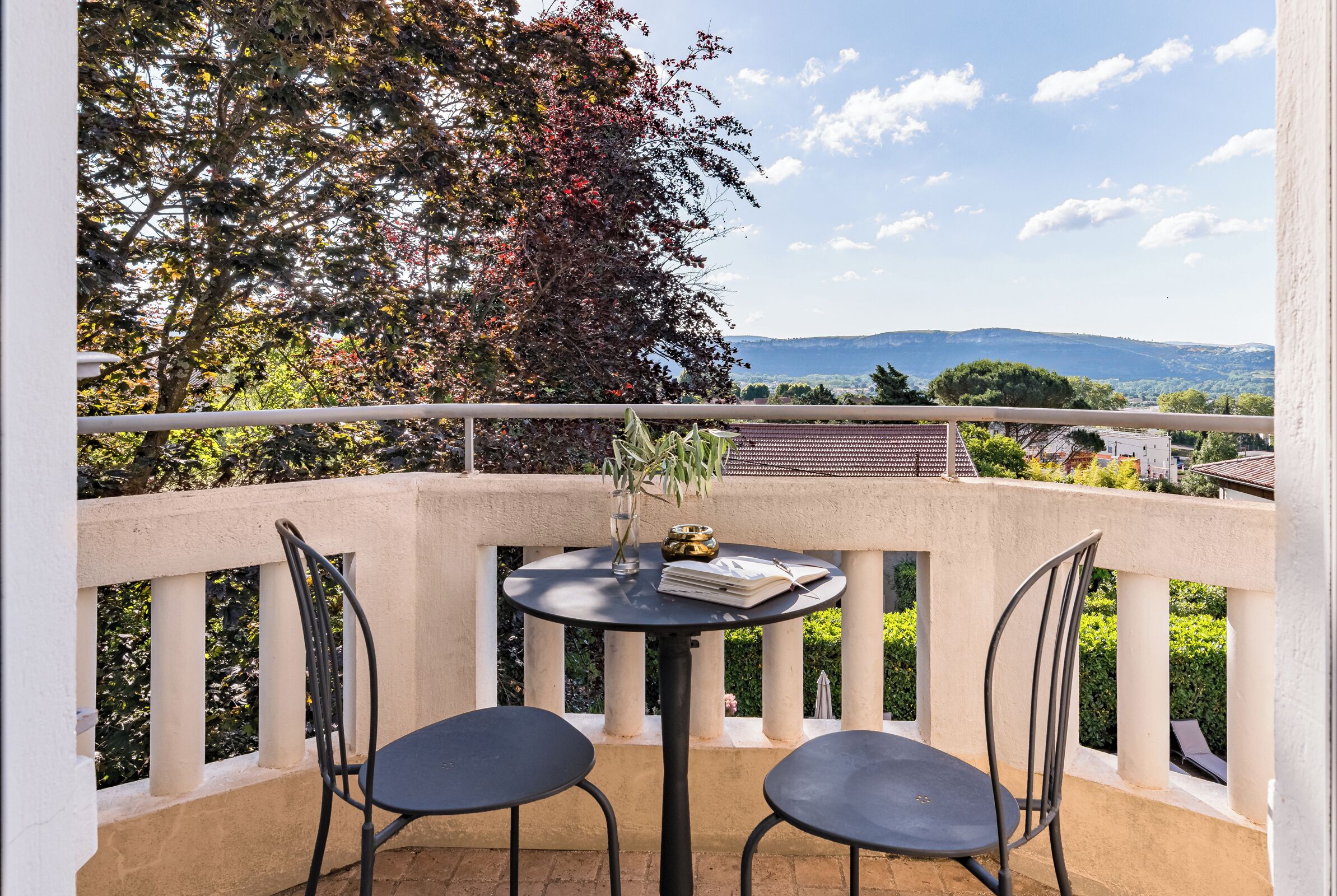 Un balcon avec deux chaises et une table, un vase et un livre.
