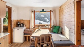 A compact room with a wooden interior, a dining table, a sofa, a small kitchenette, and a window with a snowy mountain view.