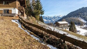 A wooden cabin with a balcony, a wooden fence, and a view of snow-covered mountains.