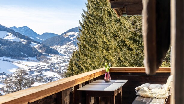 A wooden deck with a table and a chair, overlooking a snowy landscape and mountains.