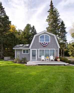 Une maison dotée d’un porche abrité, d’un petit garage attenant et d’un jardin devant avec une pelouse et des arbres.