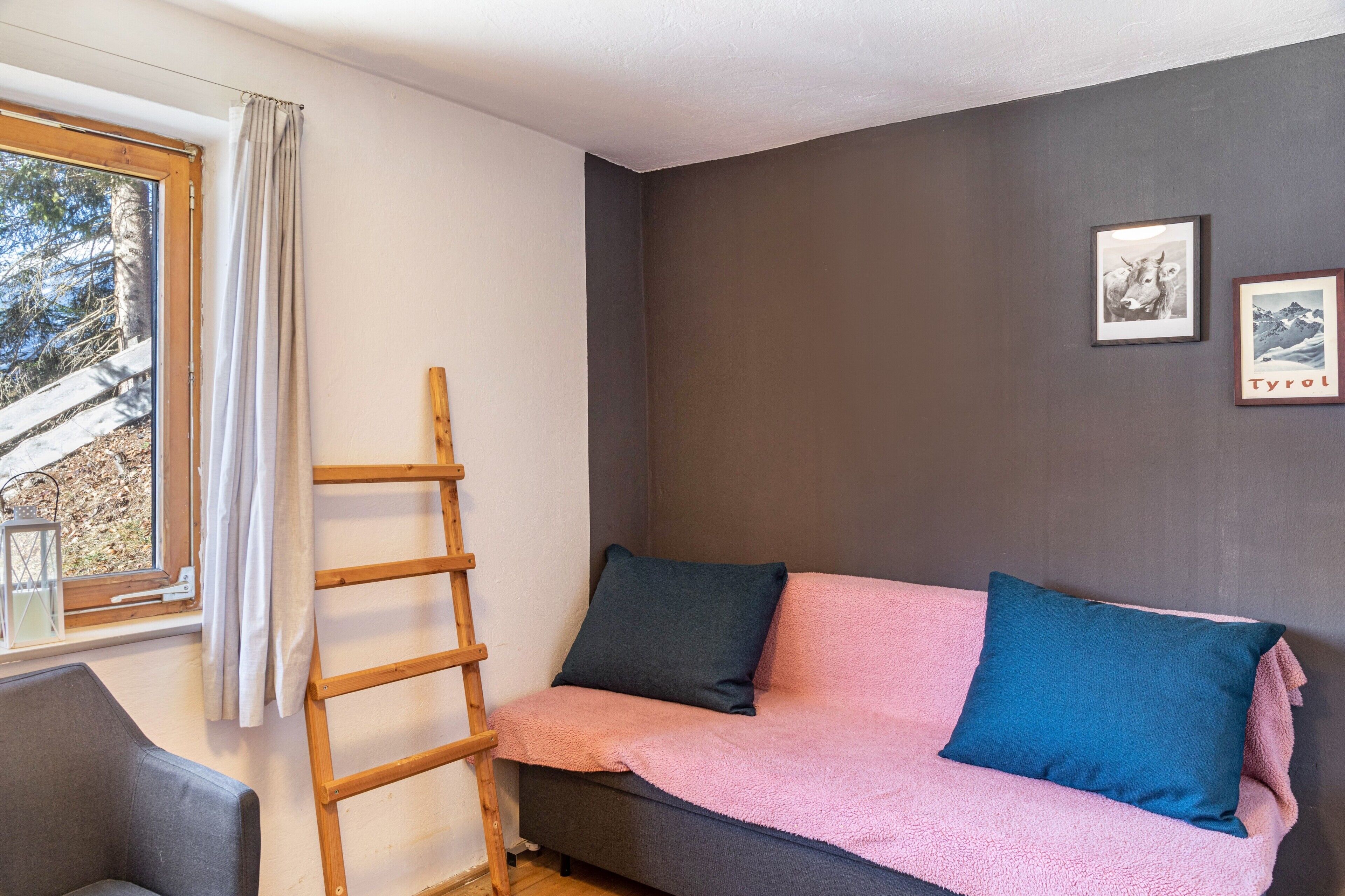 Une pièce comprenant un canapé, une échelle en bois, une fenêtre avec des rideaux et deux tableaux encadrés accrochés au mur.