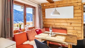 A cozy room with a wooden wall, a dining table, a bench, and a view of mountains.