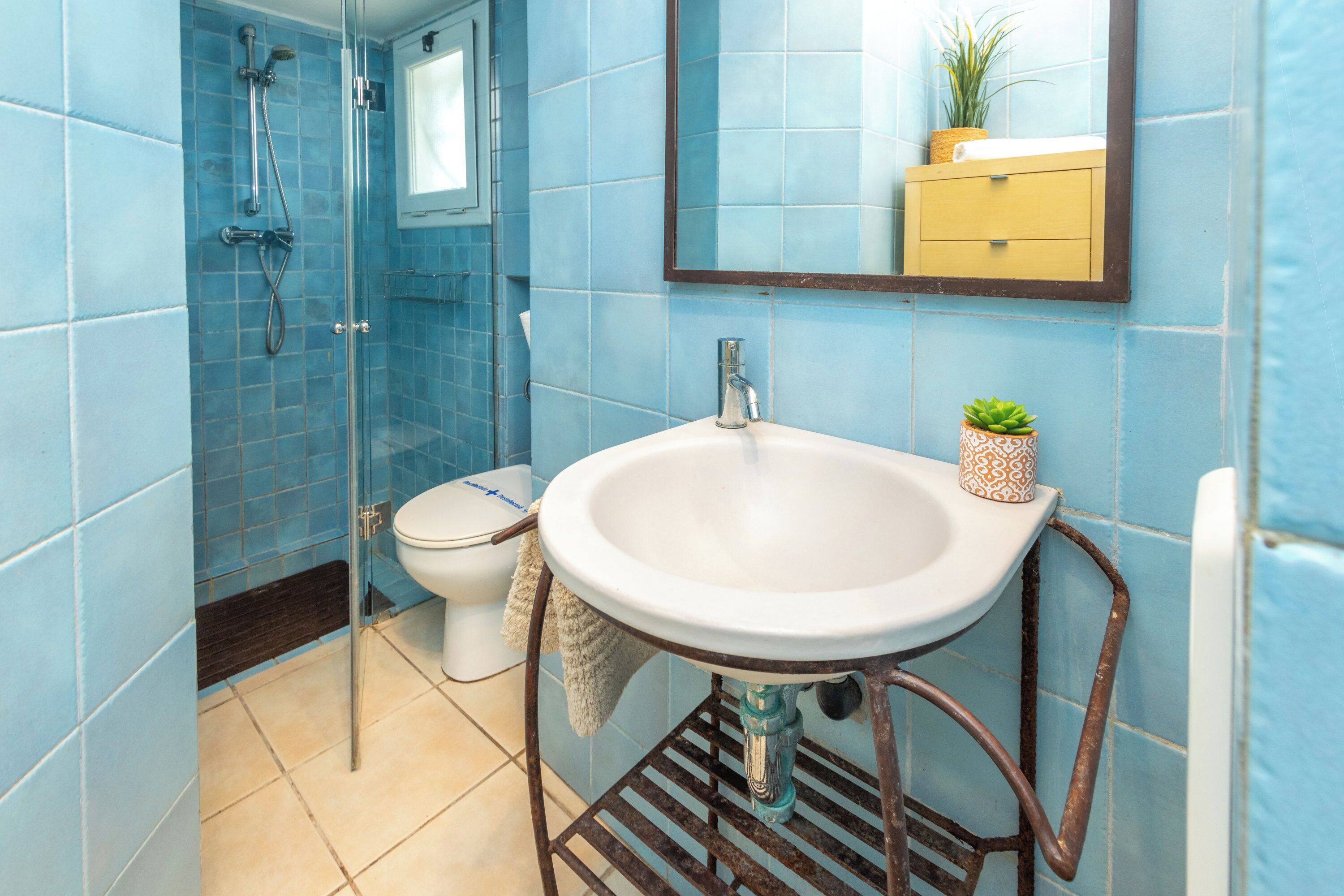 A bathroom with blue tiles, a white sink, a mirror, a shower, and a toilet.