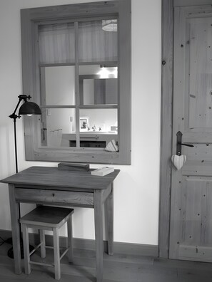 A room with a wooden desk, a chair, a desk lamp, a mirror, and a door.