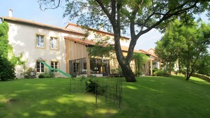 Une maison avec un toboggan vert, un espace de jeux clôturé et un grand arbre dans le jardin.