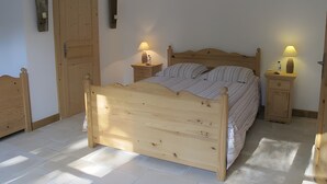 Un lit en bois, avec deux tables de chevet, chacune équipée d’une lampe, dans une pièce dotée d’une grande porte en bois et d’une petite étagère fixée au mur.