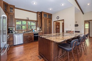 A kitchen with wooden cabinets, a large island with bar stools, and a clock on the wall. - Experience the Ultimate Luxury Retreat on the Little Pigeon River (Sevierville)