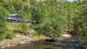 Una casa con balcón que da a un río, rodeada de un bosque denso.