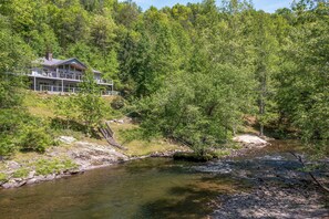 A house with a balcony overlooking a river, surrounded by dense forest. - Experience the Ultimate Luxury Retreat on the Little Pigeon River (Sevierville)