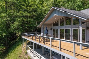 A modern house with a wooden deck, large windows, and a balcony overlooking a forested area. - Experience the Ultimate Luxury Retreat on the Little Pigeon River (Sevierville)