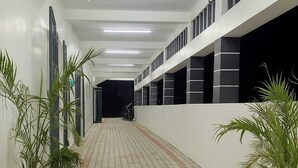 A corridor with patterned paving, potted plants, and a series of windows on the walls. - Kumbha Nivas (Kumbakonam)