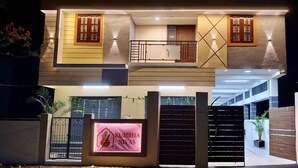 A modern two-story house with a balcony, a well-lit entrance, and a signboard. - Kumbha Nivas (Kumbakonam)
