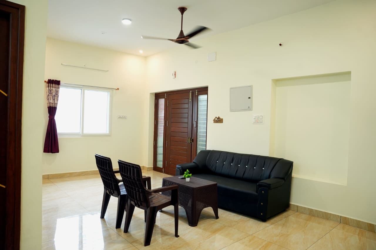 A living room with a black sofa, two chairs, a coffee table, a ceiling fan, and a door with glass panels.