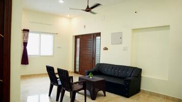 A living room with a black sofa, two chairs, a coffee table, a ceiling fan, and a door with glass panels.
