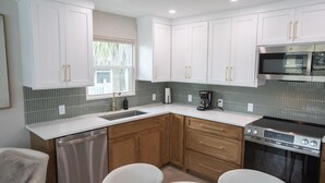 A modern kitchen with white cabinets, a stainless steel dishwasher, a coffee maker, and a stove. - The Finn at Coconut Cove (Fort Myers Beach)